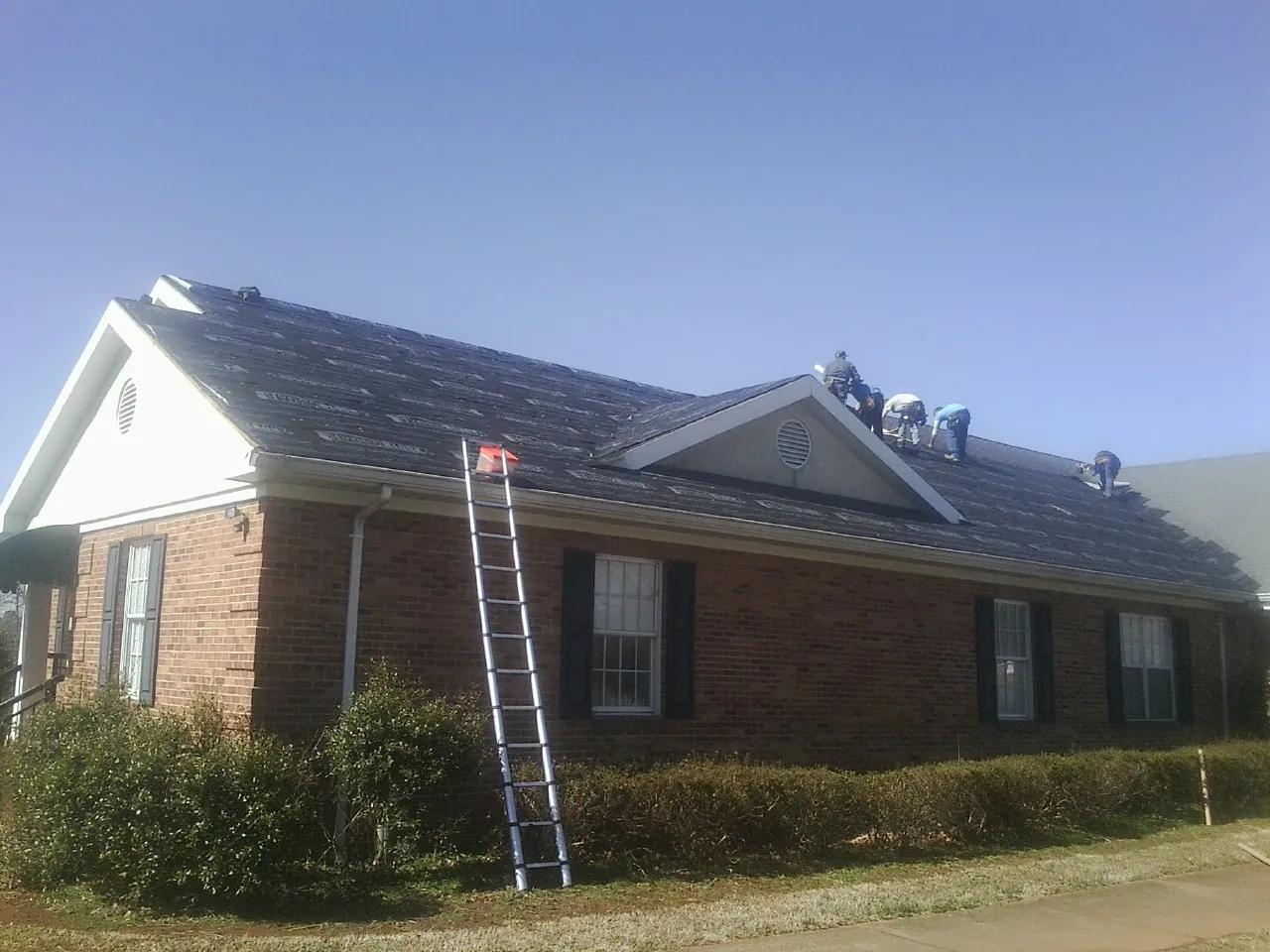 Crew tearing shingles off a brick ranch roof with a ladder set — Emergency Roof Repair work by our crew in Lincolnshire