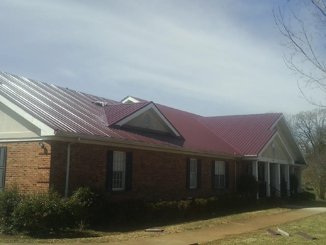 Red metal roof with gabled entries on a long brick building, from a Hail Damage Roof Repair job in Lincolnshire
