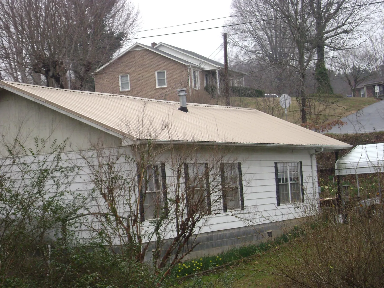 Tan metal roof on a white sided house set into a hillside — Commercial Roofing by Roofing Brothers in Lincolnshire